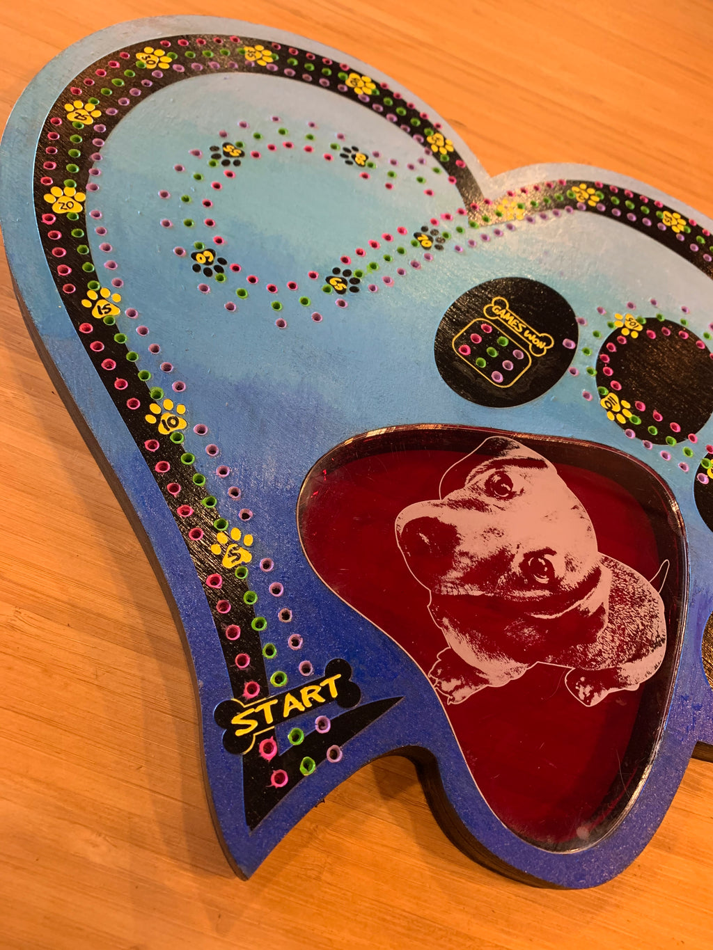 Decorative game board with a dog illustration and colorful border on a wooden surface