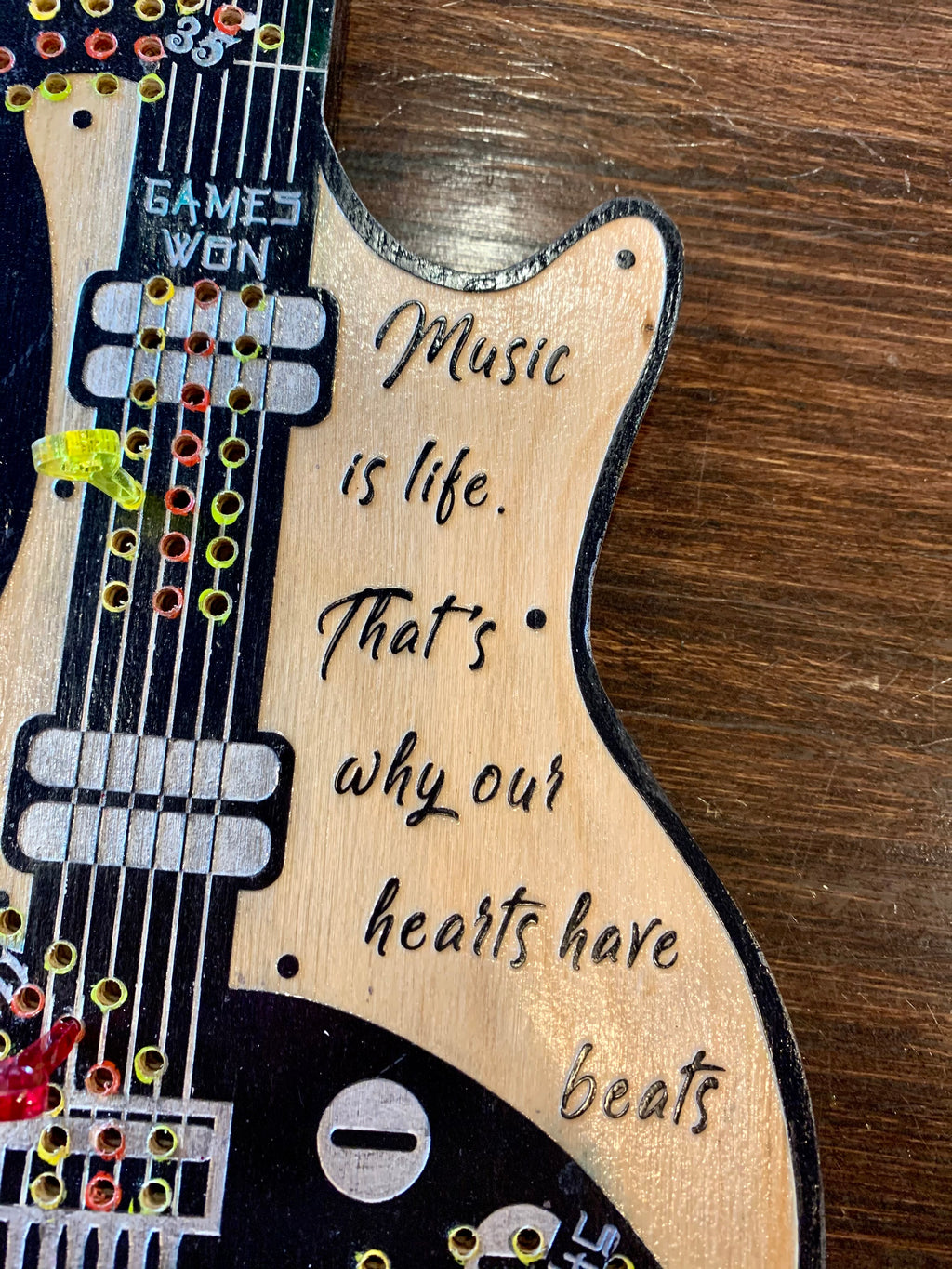 Wooden guitar shaped cribbage board with engraved text on a wooden surface