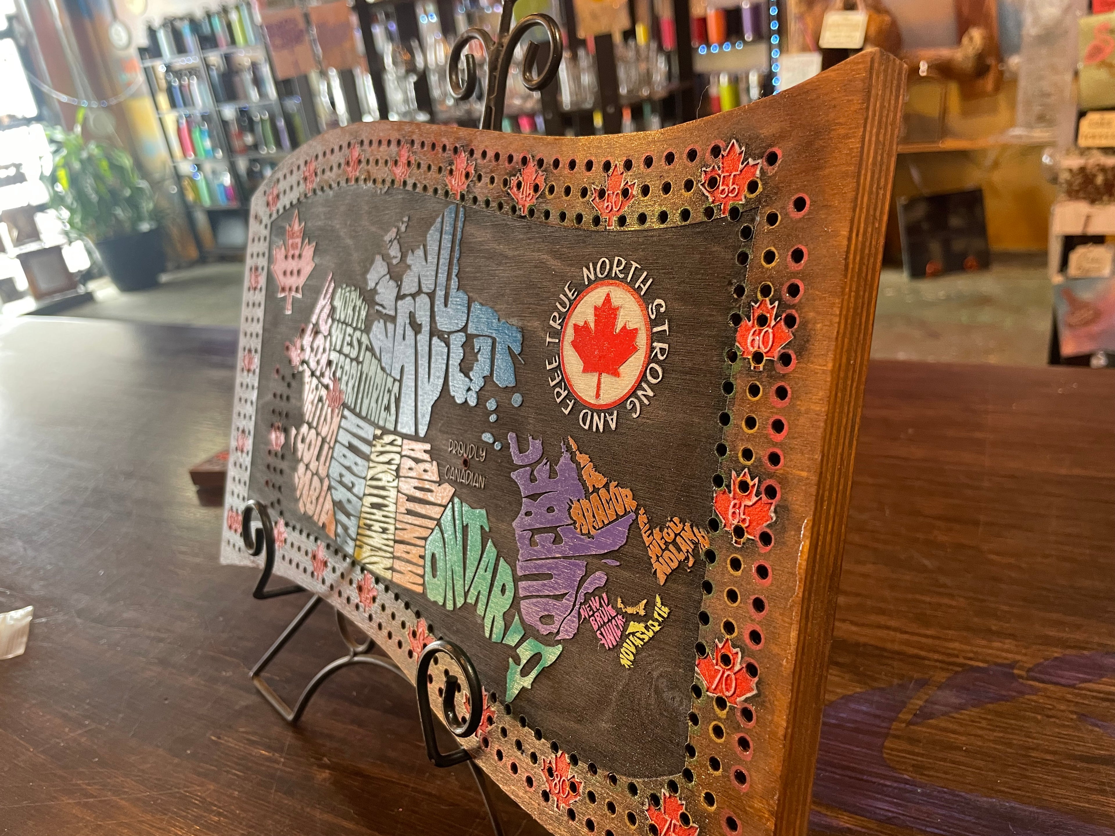 Map of Canada with colorful provinces on a wooden cribbage board with decorative elements.
