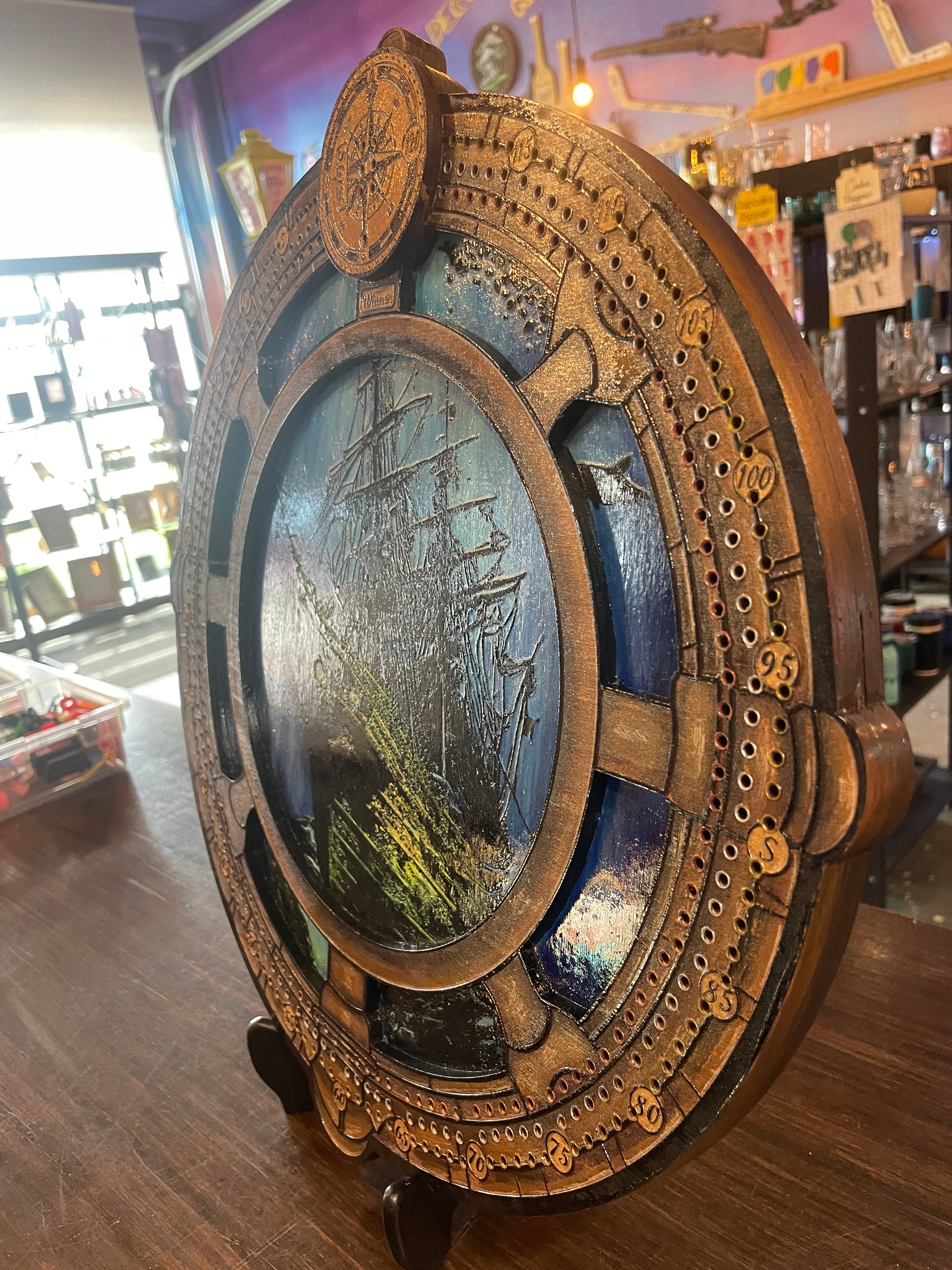 Decorative compass and ship wheel cribbage board with sunken ship.