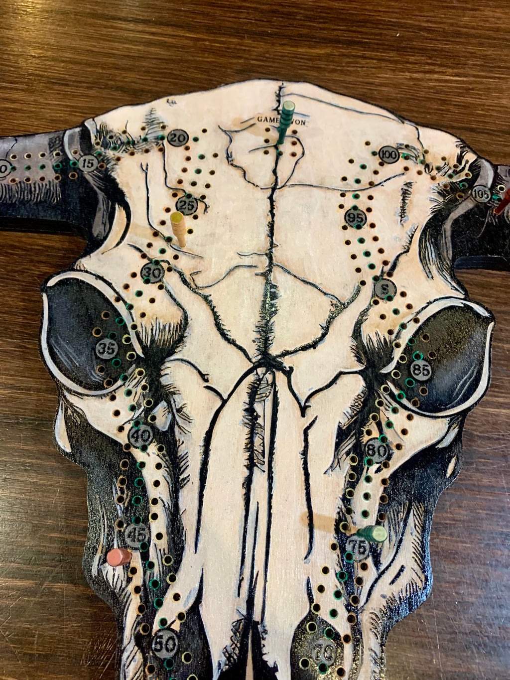 Decorative cow skull with artistic designs on a wooded cribboard.