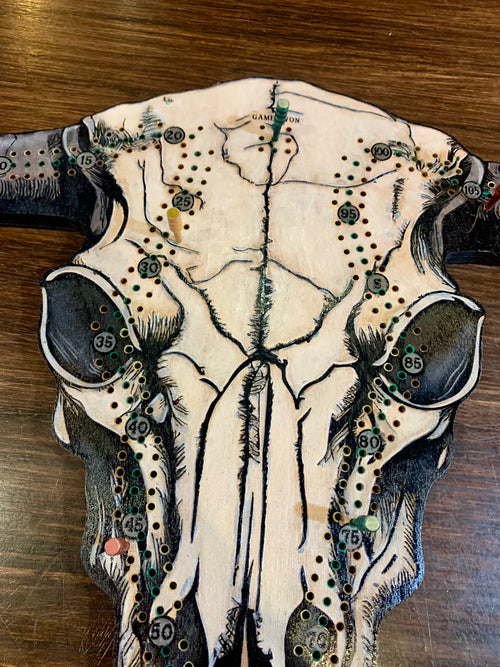 Decorative cow skull with artistic designs on a wooded cribboard.