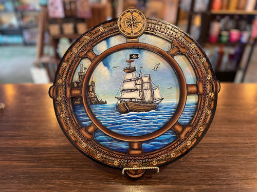Decorative compass with ship and lighthouse illustration on a cribboard.