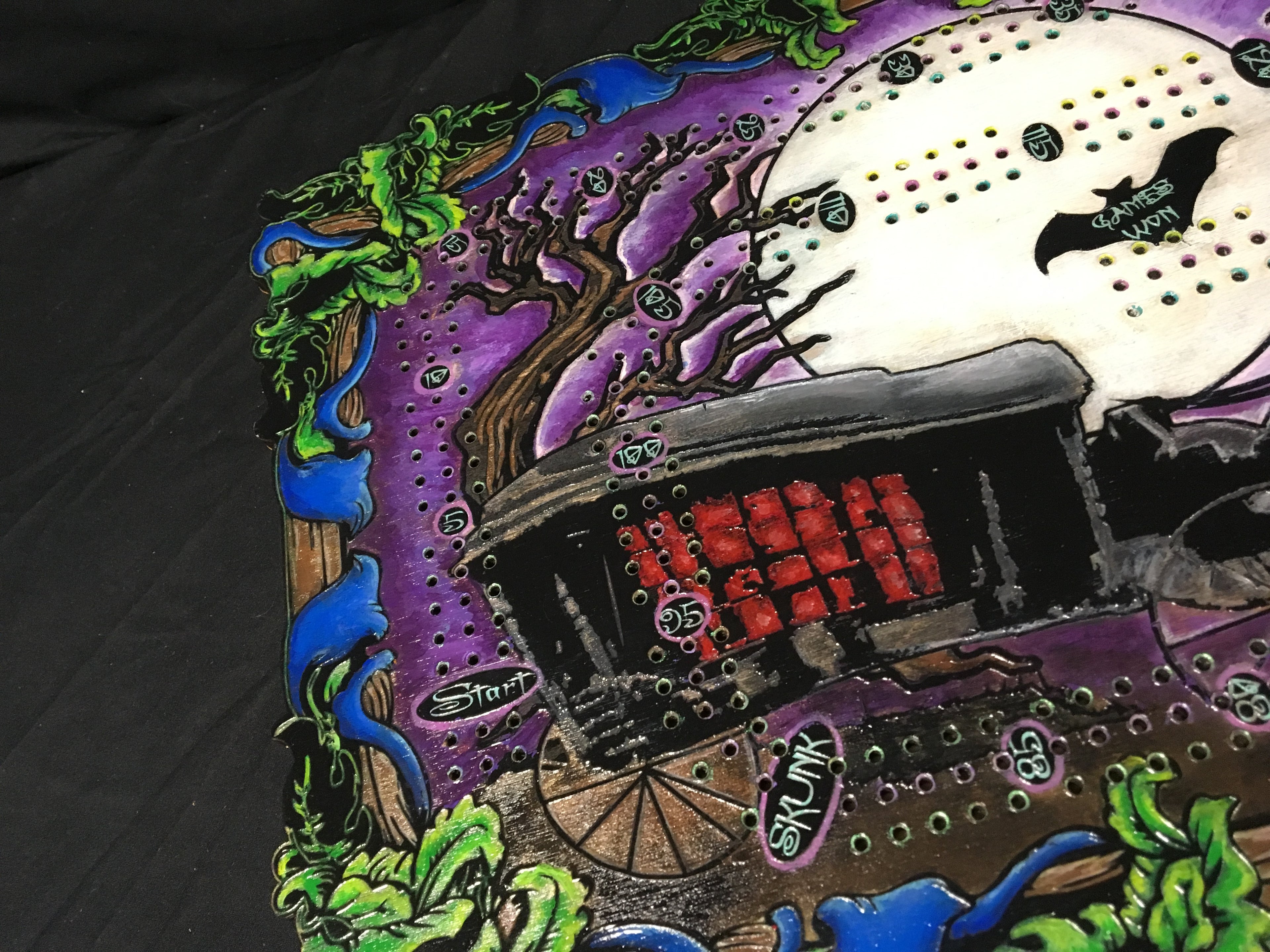 Colorful hand painted design on a black background featuring a haunted house and moon.