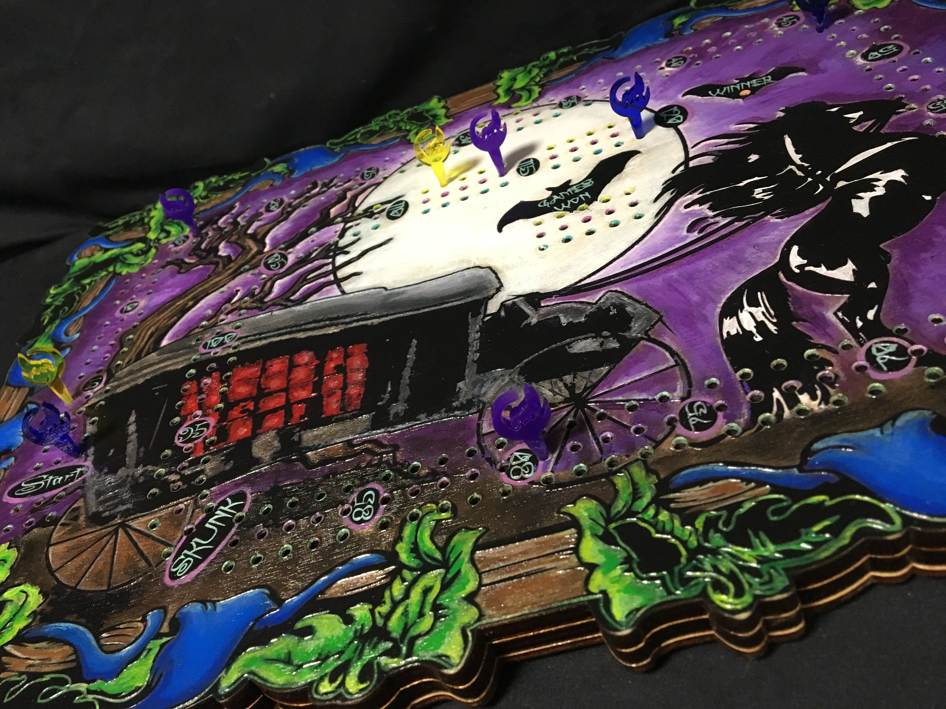 Halloween-themed cribbage board with a carriage, moon, and bats on a purple background.