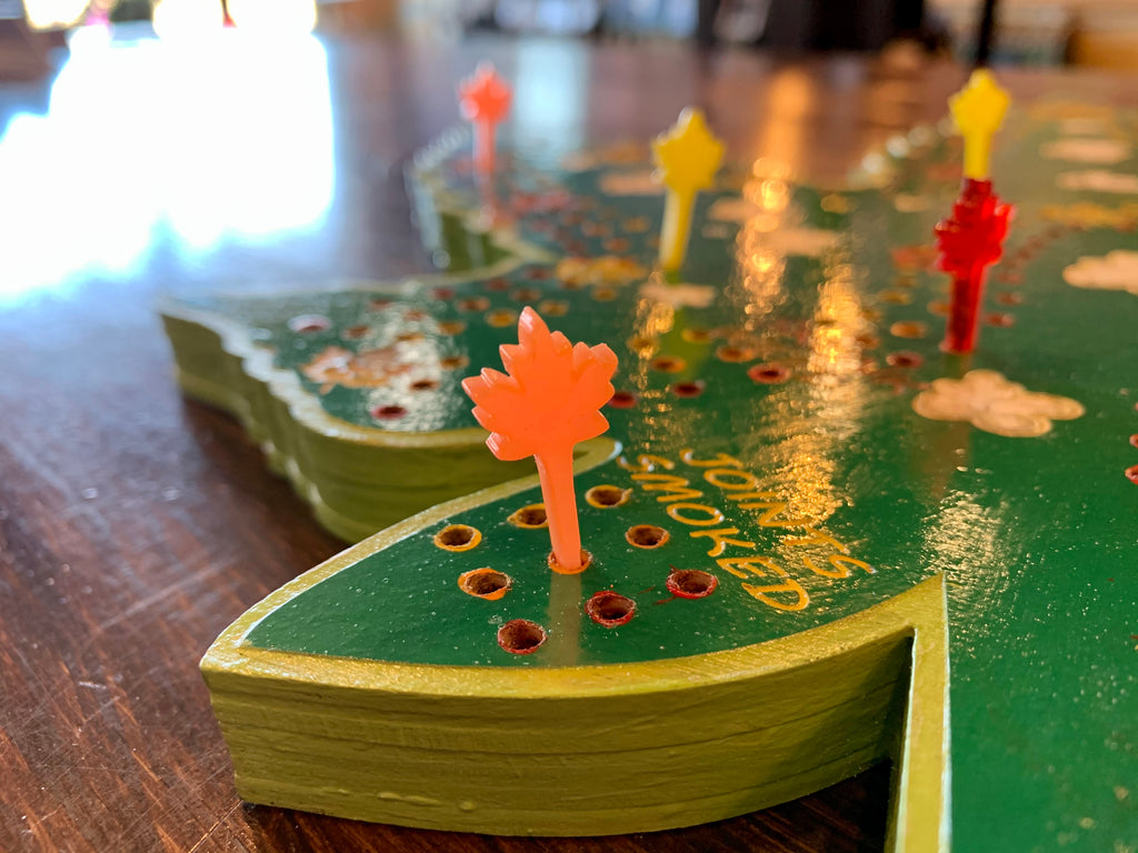 Close-up of a green wooden cribbage board with holes and colorful acrylic pegs.