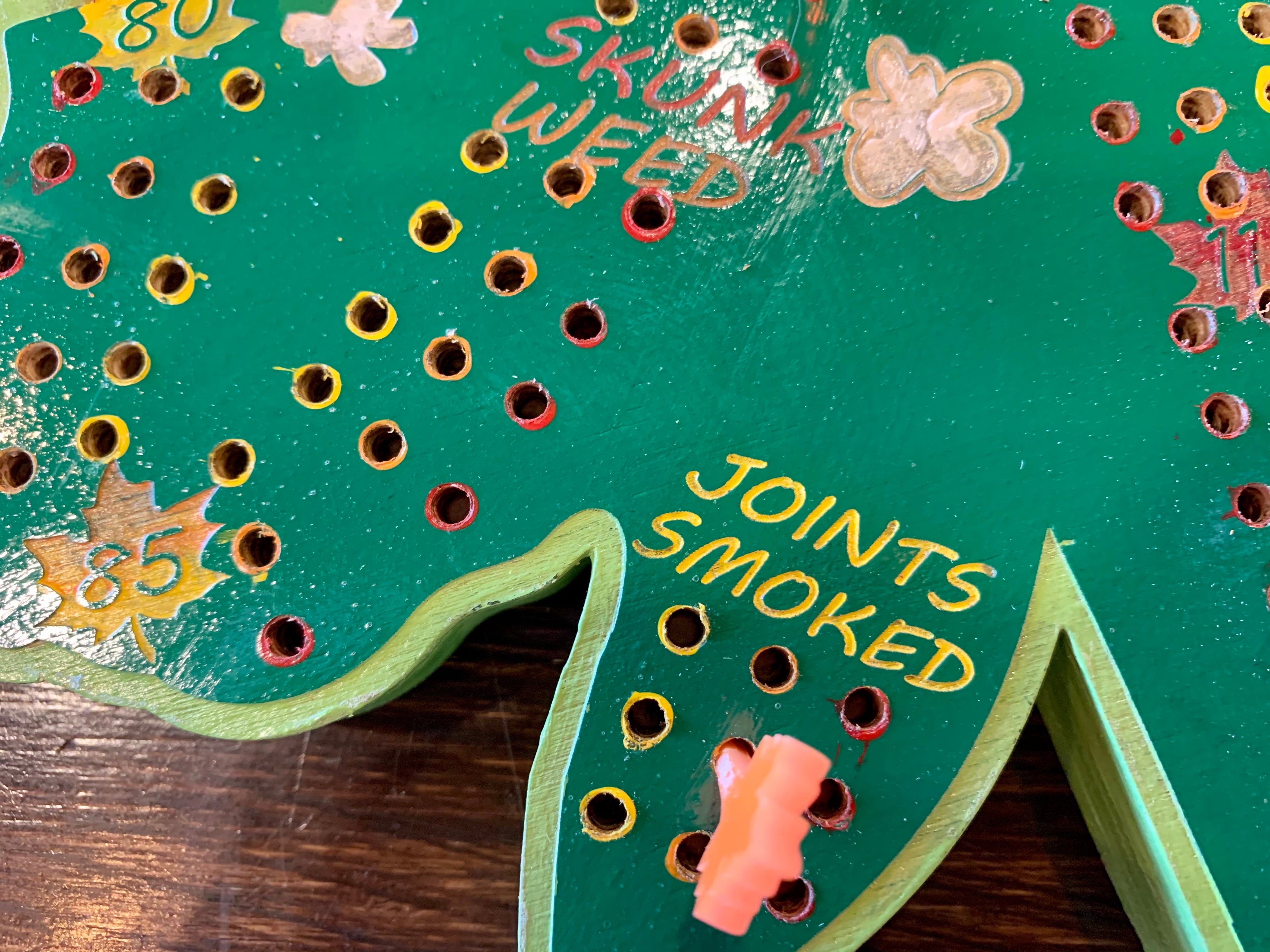 Close-up of a green wooden cribbage board with holes and colorful acrylic pegs.
