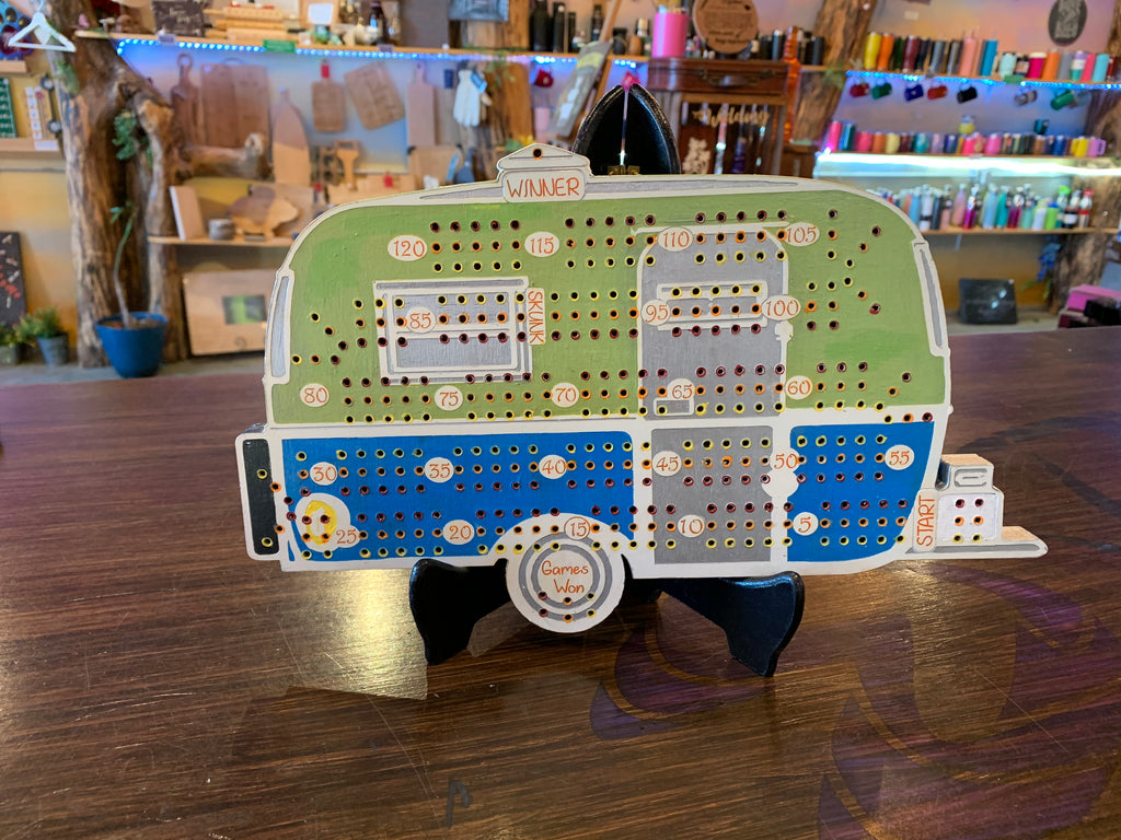Cribbage board shaped like a camper on a wooden floor with a store in the background