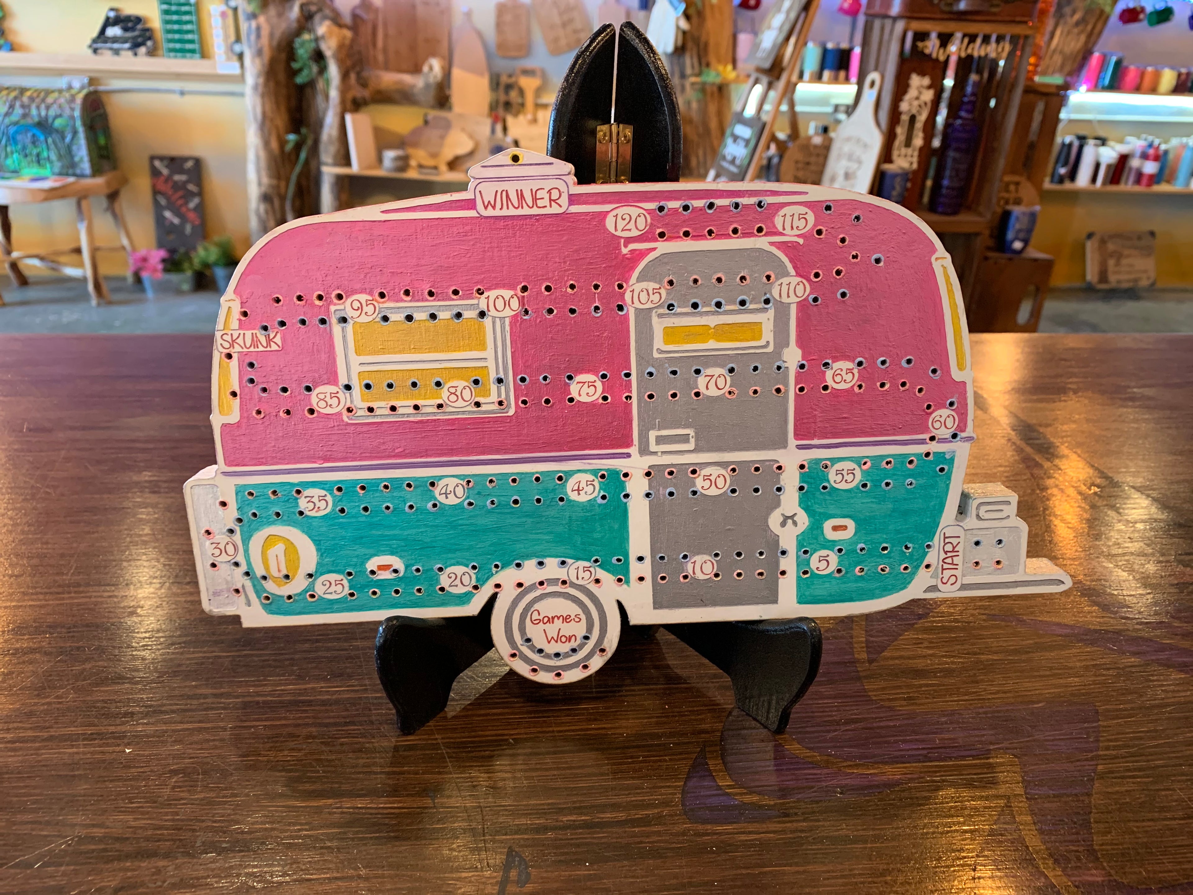 Colorful cribbage board shaped like a camper on a wooden surface.